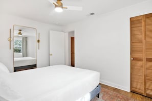 Une chambre à coucher avec un lit, un ventilateur de plafond, un miroir et une porte en bois.