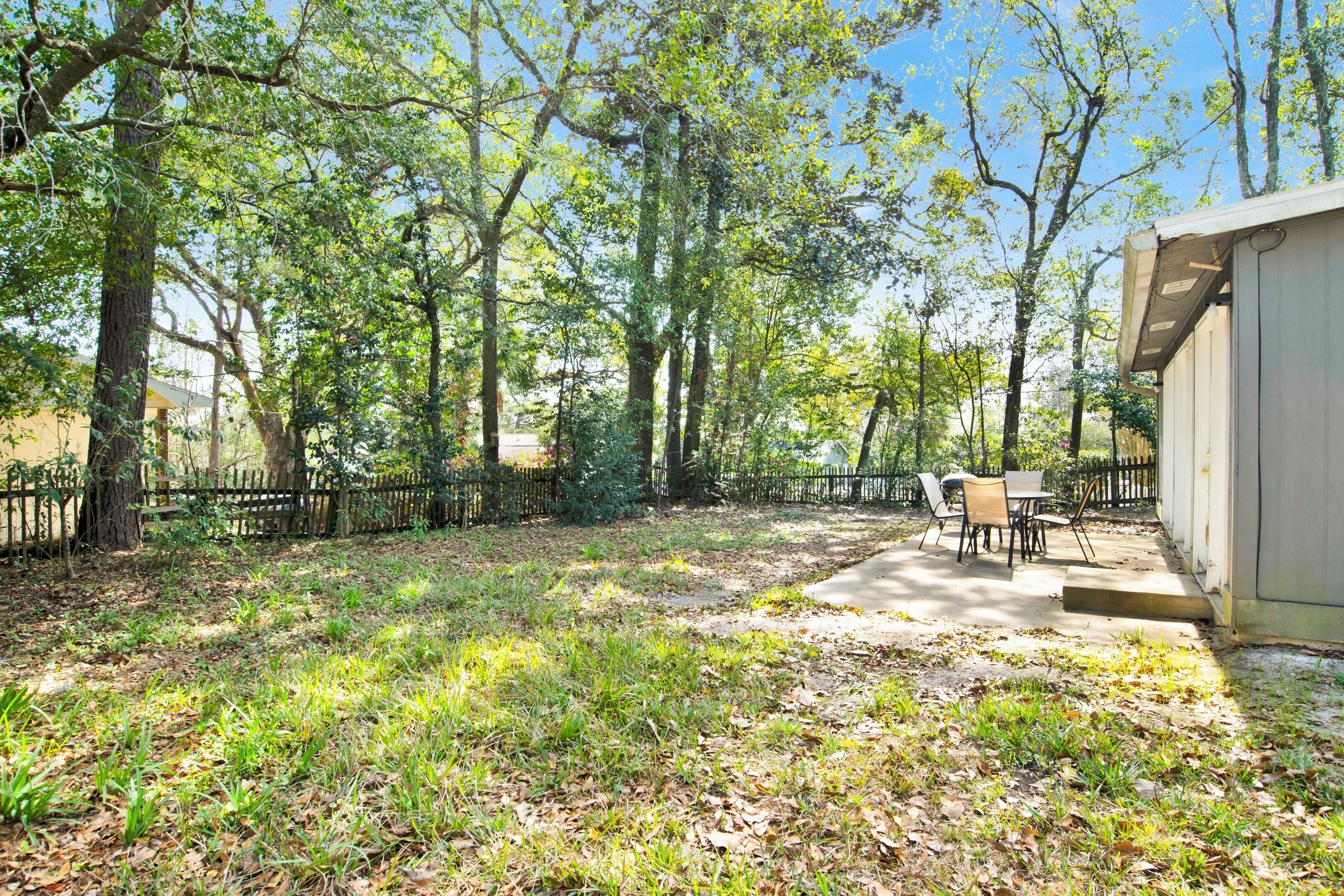 A backyard with a patio, a table, and chairs. There is a fence and trees surrounding the area.
