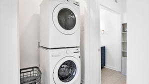 A stacked washer and dryer unit in a hallway with a door and a small storage unit in the background.