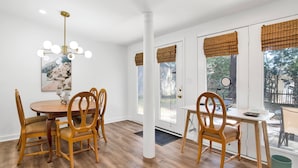 A dining area with a round table, wooden chairs, a chandelier, and large windows with blinds. - Cozy 2BR Spring Hill Cottage • Pets Welcome (Mobile)