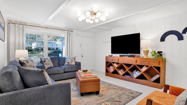 A modern living room with a grey sofa, a wooden coffee table, and a TV stand with books.