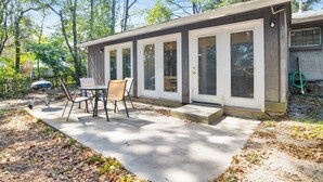 A covered patio with a table and chairs, a barbecue grill, and a house with large windows. - Cozy 2BR Spring Hill Cottage • Pets Welcome (Mobile)