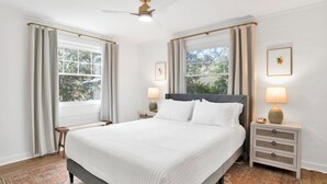 A bedroom with a large bed, two bedside tables with lamps, a ceiling fan, and windows with curtains. - Cozy 2BR Spring Hill Cottage • Pets Welcome (Mobile)