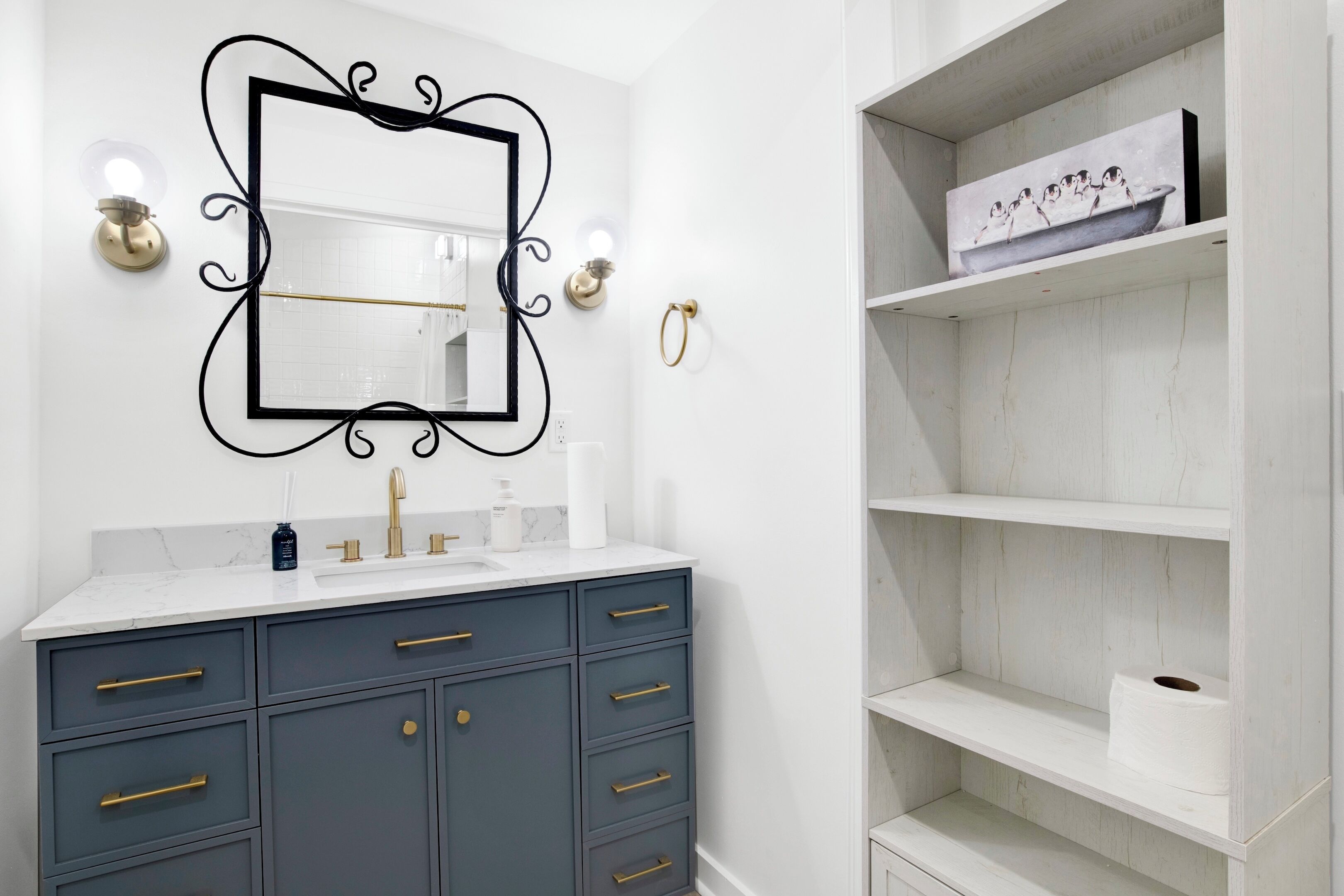 Un bagno con un mobile lavabo bianco, armadietti blu scuro, un rubinetto dorato e uno specchio con cornice nera decorata.