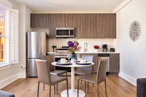A modern kitchen with a built-in microwave, a stainless steel refrigerator, and a dining area with a round table and four chairs. - The Penn Hotel - 2BR Above Nightlife & Top Clubs!! (San Diego)