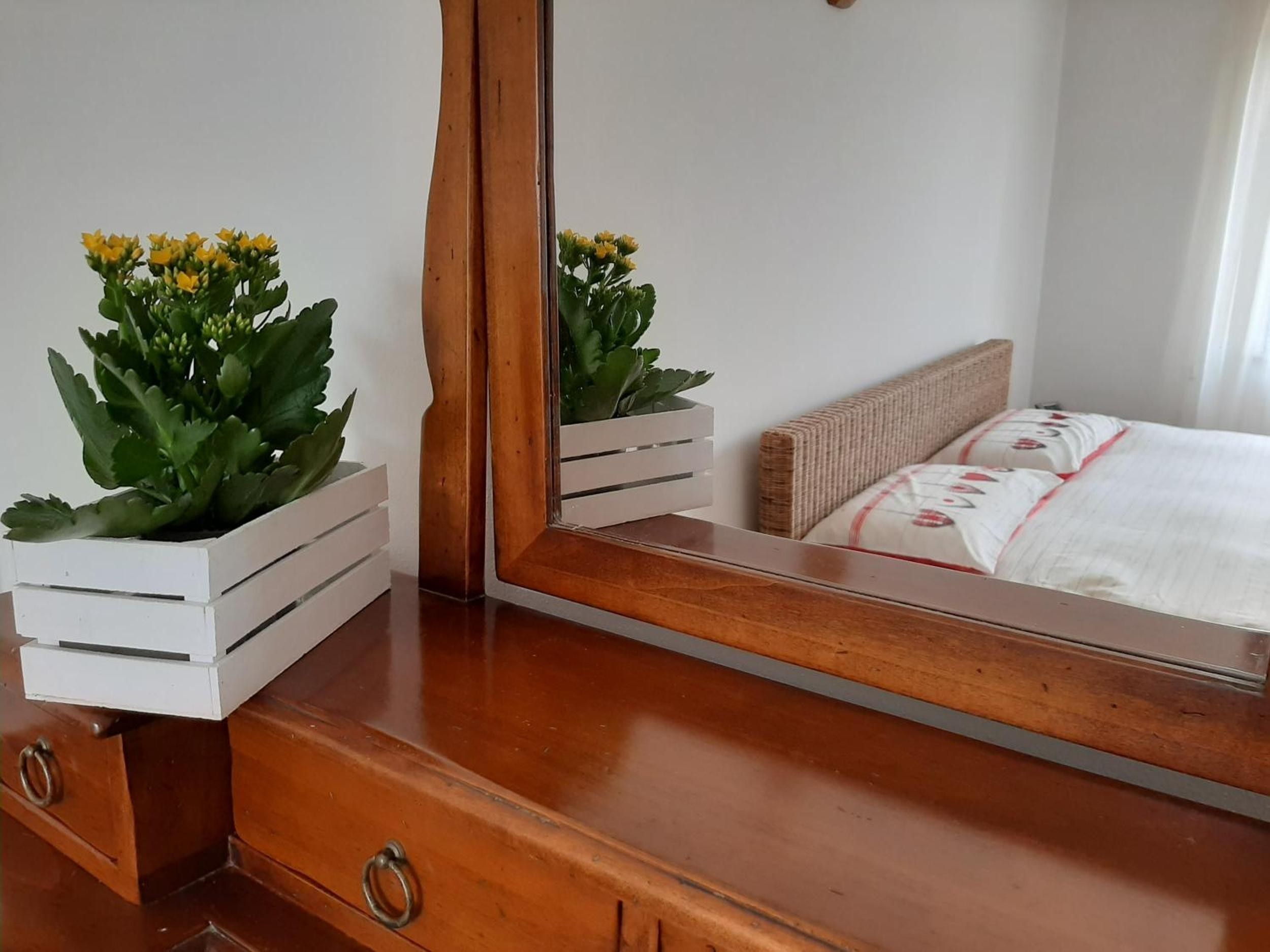 Une commode en bois, dotée de tiroirs et d’un miroir qui reflète un lit recouvert d’une couvre-lit à motifs blancs et rouges.