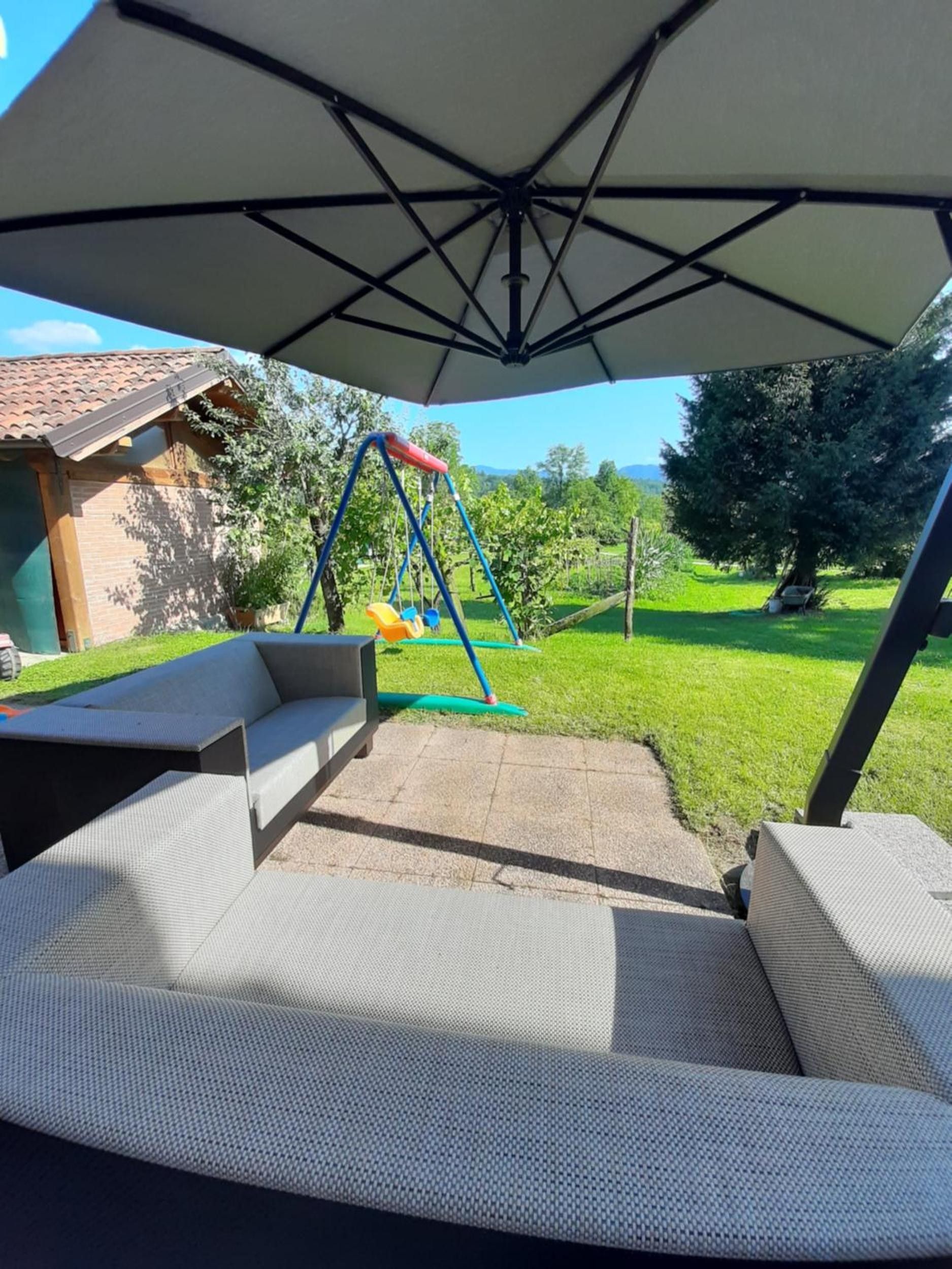 Un espace extérieur aménagé en terrasse, avec une balançoire, un coin salon abrité et une vue sur un paysage verdoyant.