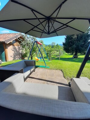 An outdoor patio area with a swing set, a covered seating area, and a view of a green landscape.