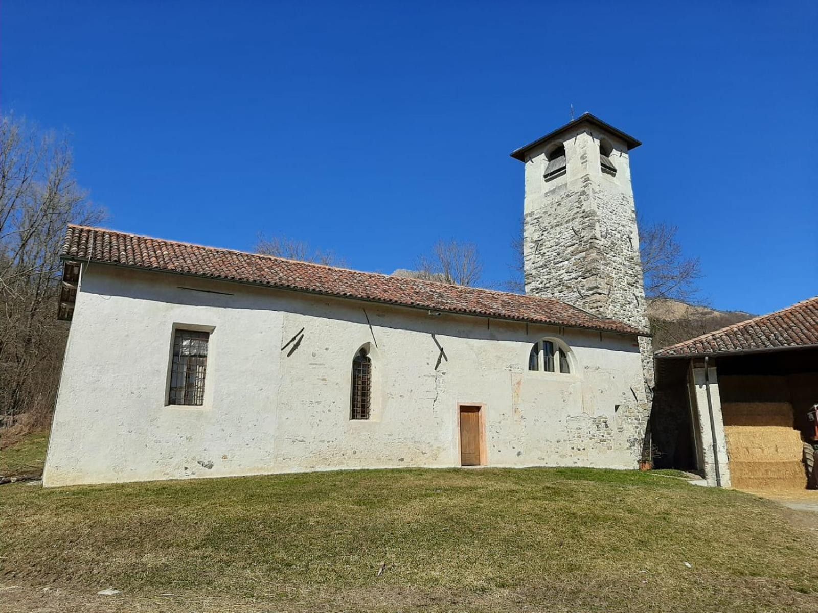 Un bâtiment blanc avec une tour en pierre, un toit recouvert de tuiles et une pelouse devant.