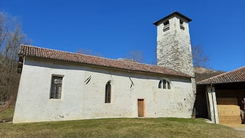 Un bâtiment blanc avec une tour en pierre, un toit recouvert de tuiles et une pelouse devant.