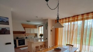 A dining area with a wooden table and chairs, a kitchen in the background, and a window with curtains. - Country House 'San Marcello Residence' with Mountain View, Private Garden and Wi-Fi (Villabruna-umin)