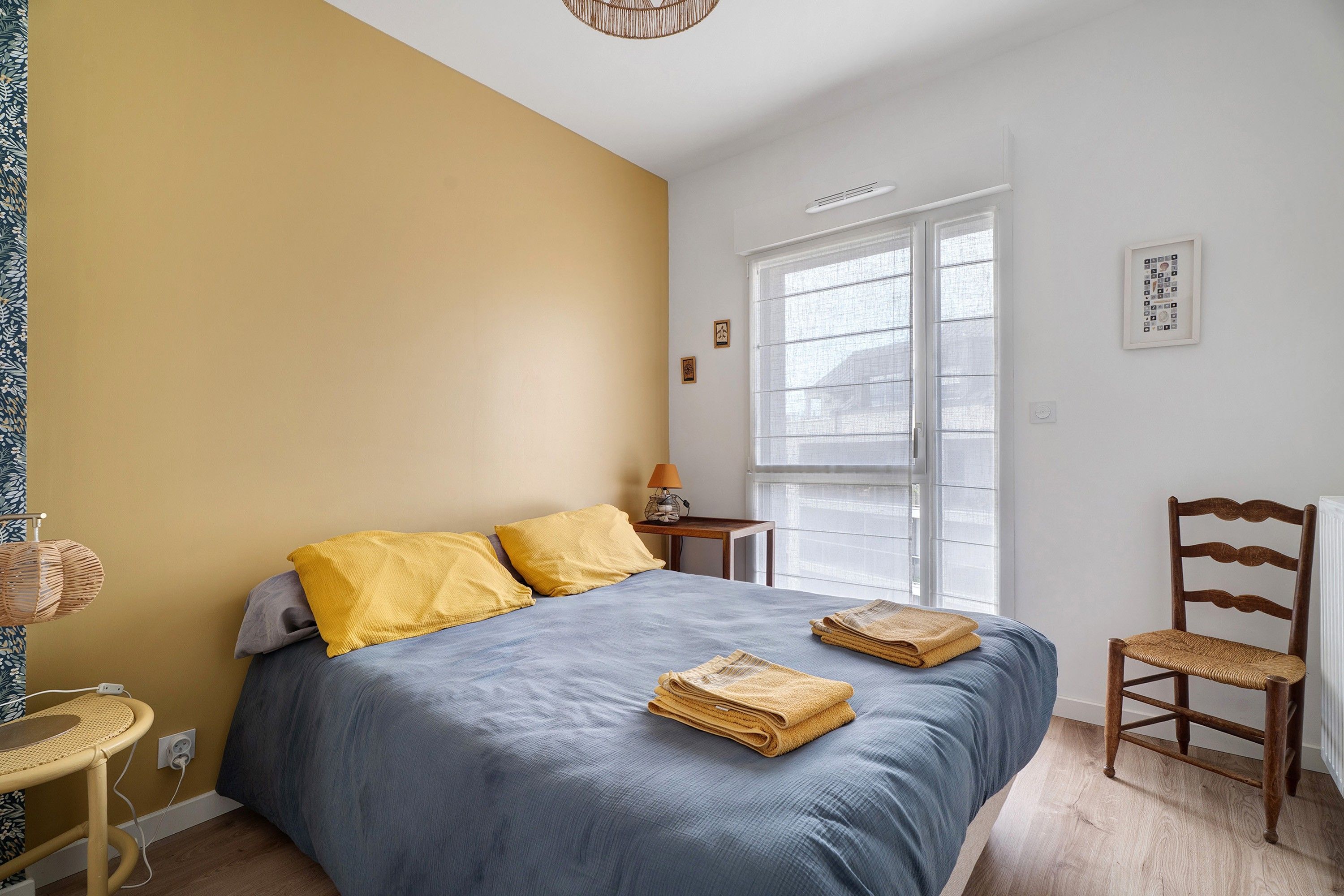 Ein Schlafzimmer mit einem Bett, einem Sessel, einer Lampe und einem Fenster.
