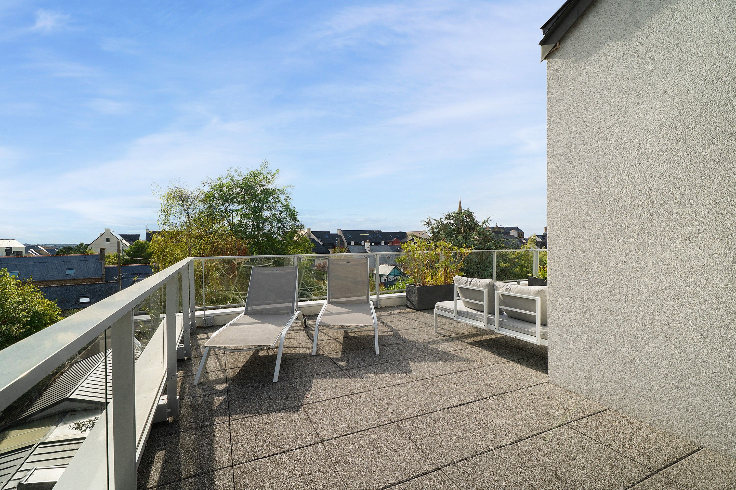 Eine Dachterrasse mit zwei Stühlen, einem Tisch, einer Brüstung und Blick auf die umliegenden Gebäude.