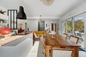 Et moderne køkken med en træø, et spiseområde med et stort bord, og en lys stue med en gul sofa.