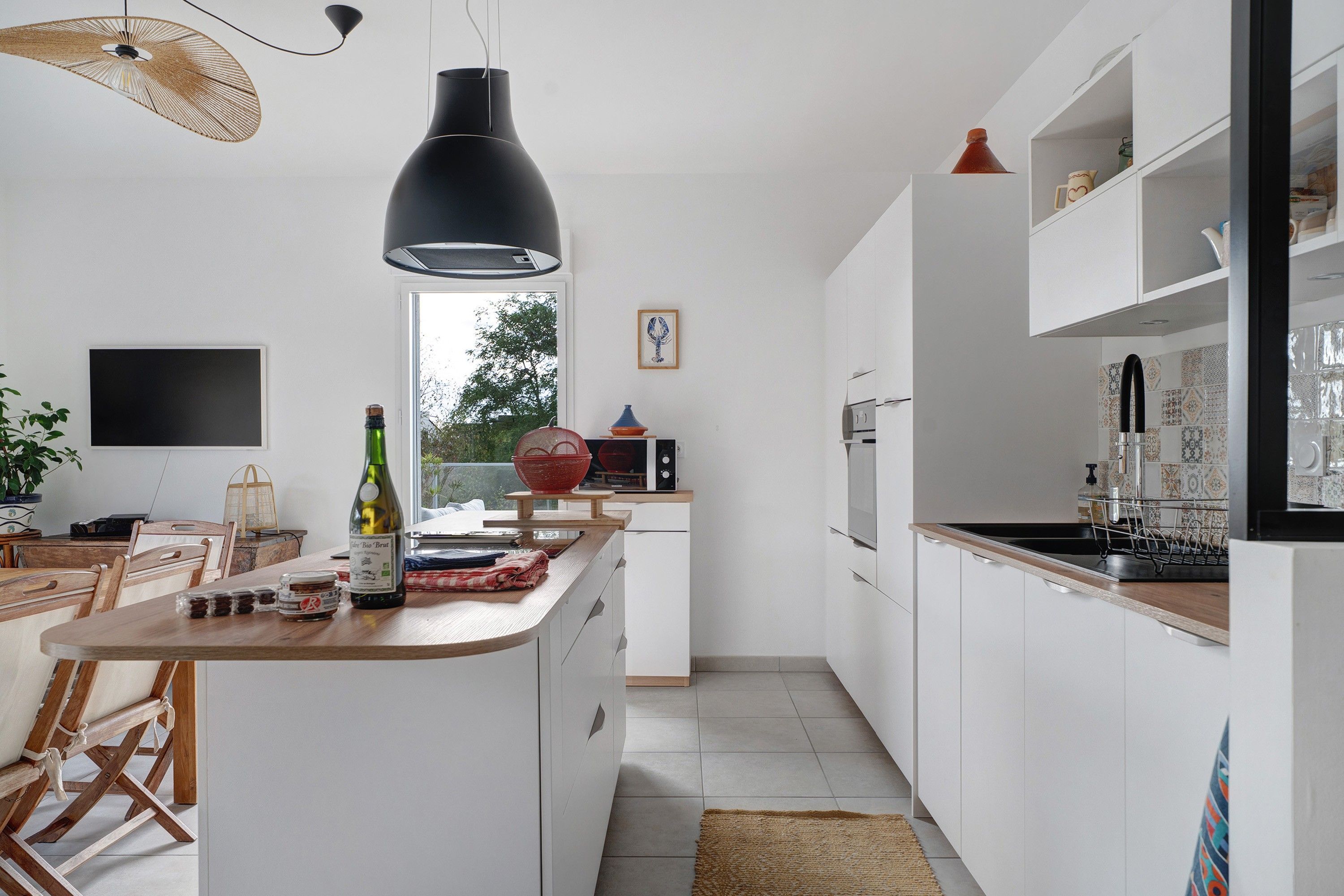 Eine moderne Küche mit weißen Schränken, einem Holztisch und einem großen Fenster.