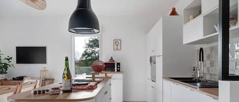 Una cocina moderna con armarios blancos, una mesa de comedor de madera y un ventanal grande.