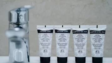 Quatre tubes de produits de toilette étiquetés « LOTION POUR LE CORPS » et « SHAMPOING ET GEL DOUCHE », avec un robinet en arrière-plan.