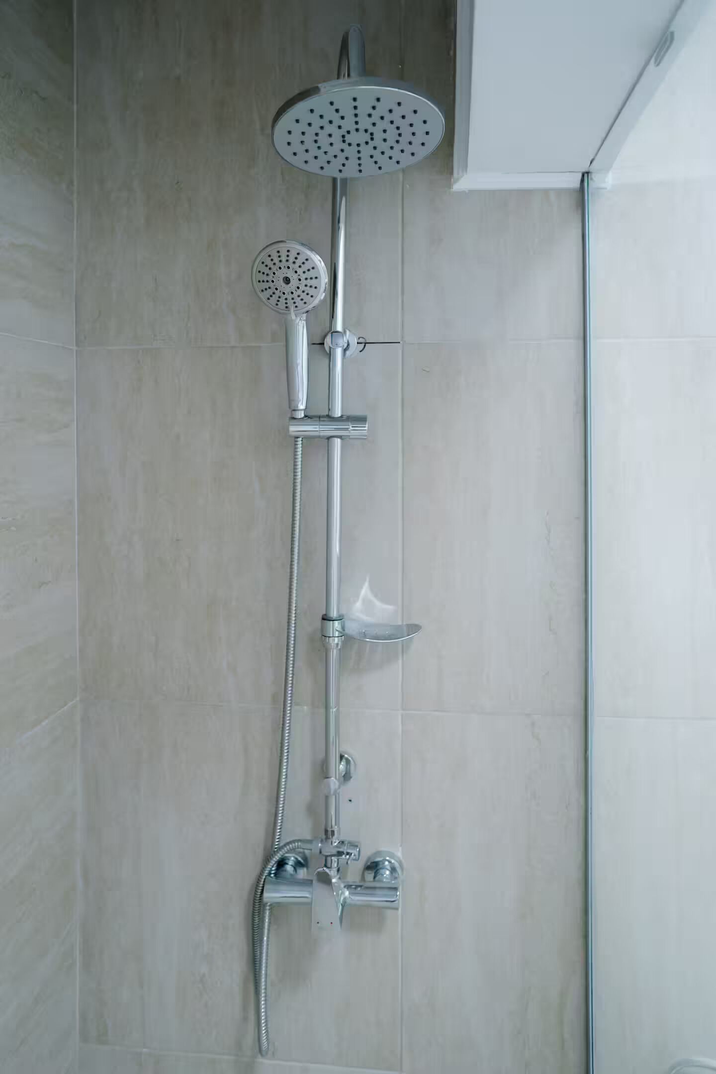 Una ducha con cabezal de ducha de mano, cabezal de ducha fijo y manguera para ducha de mano.