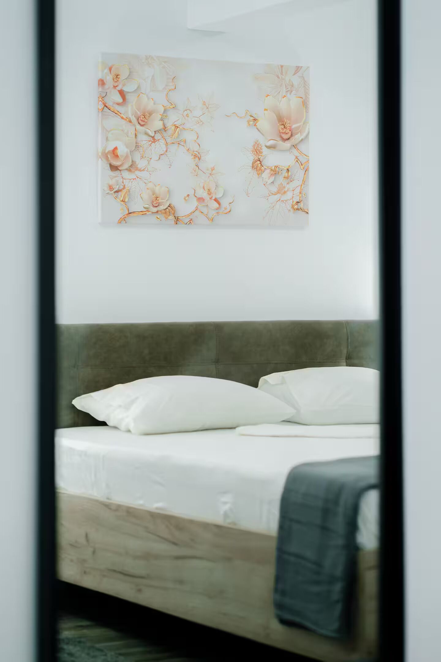 Una cama con ropa de cama blanca y un cabecero gris en una habitación con una obra de arte colgada en la pared.