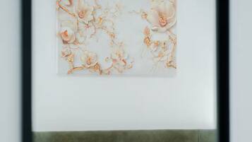Una cama con ropa de cama blanca y un cabecero gris en una habitación con una obra de arte colgada en la pared.