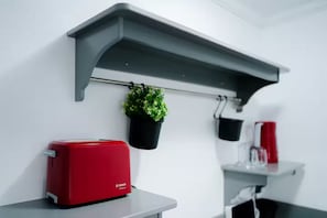 A kitchen with a red toaster on a white countertop, a grey shelf above holding a potted plant, and a red container on a lower shelf. - Cozy 1-bedroom apartment in lovely București with Ac Mavie Studio 2 (București)