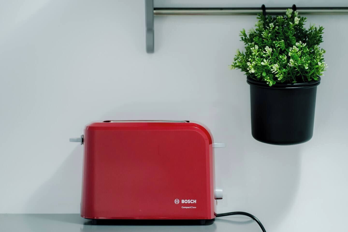 Un tostador rojo Bosch sobre una encimera blanca con una planta en maceta colgante.