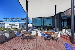 Een terras op het dak met houten vloer, blauwe rieten stoelen en tafels.