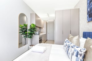 A modern bedroom with a bed, a bedside table, a mirror, a plant, and a wardrobe. - Refined City Living with Panoramic Views (Johannesburg)