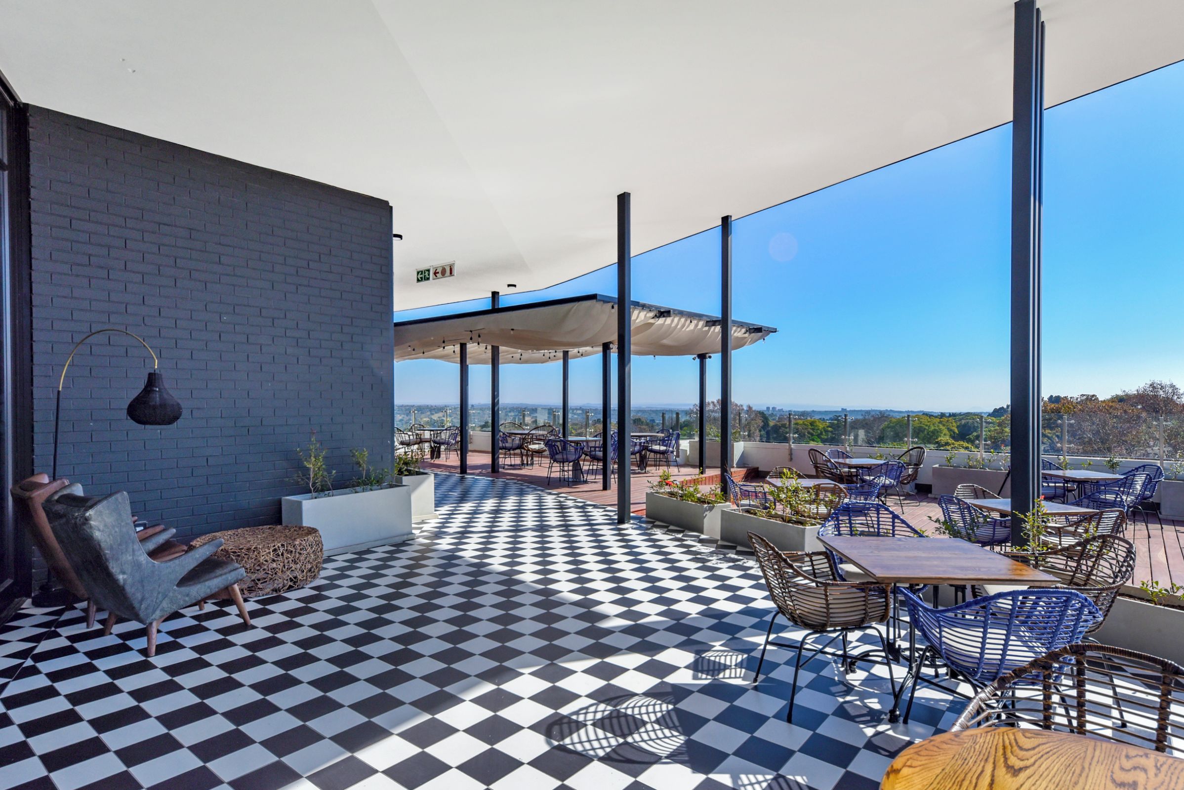 Eine Dachterrasse mit Schachbrettmuster-Boden, Sitzgelegenheiten im Freien und Blick auf die Stadt.