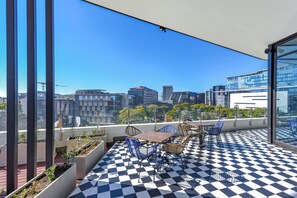 Een terras op het dak met een geruite vloer, zitplaatsen en uitzicht over de stad.