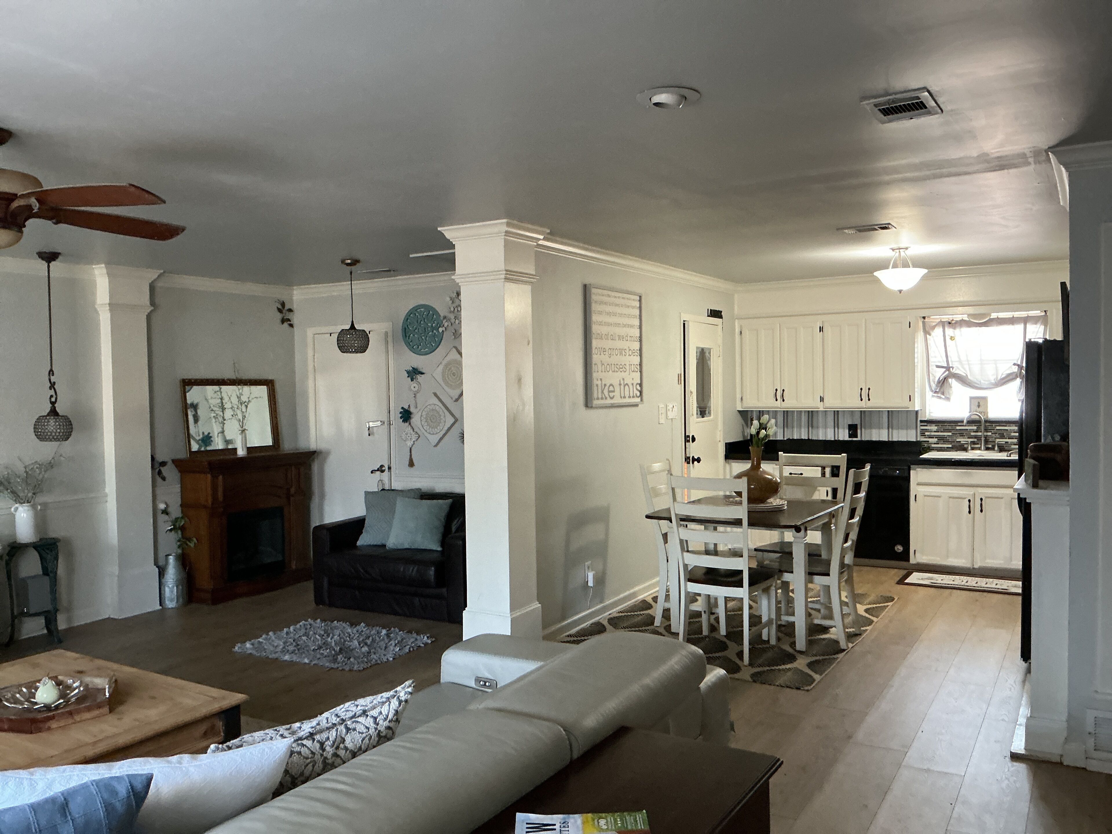 A spacious living room with a sofa, a dining table with chairs, a kitchen area with white cabinets, and a ceiling fan.