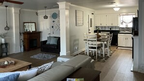 Een ruime woonkamer met een bank, een eettafel met stoelen, een keuken met witte kasten en een plafondventilator.
