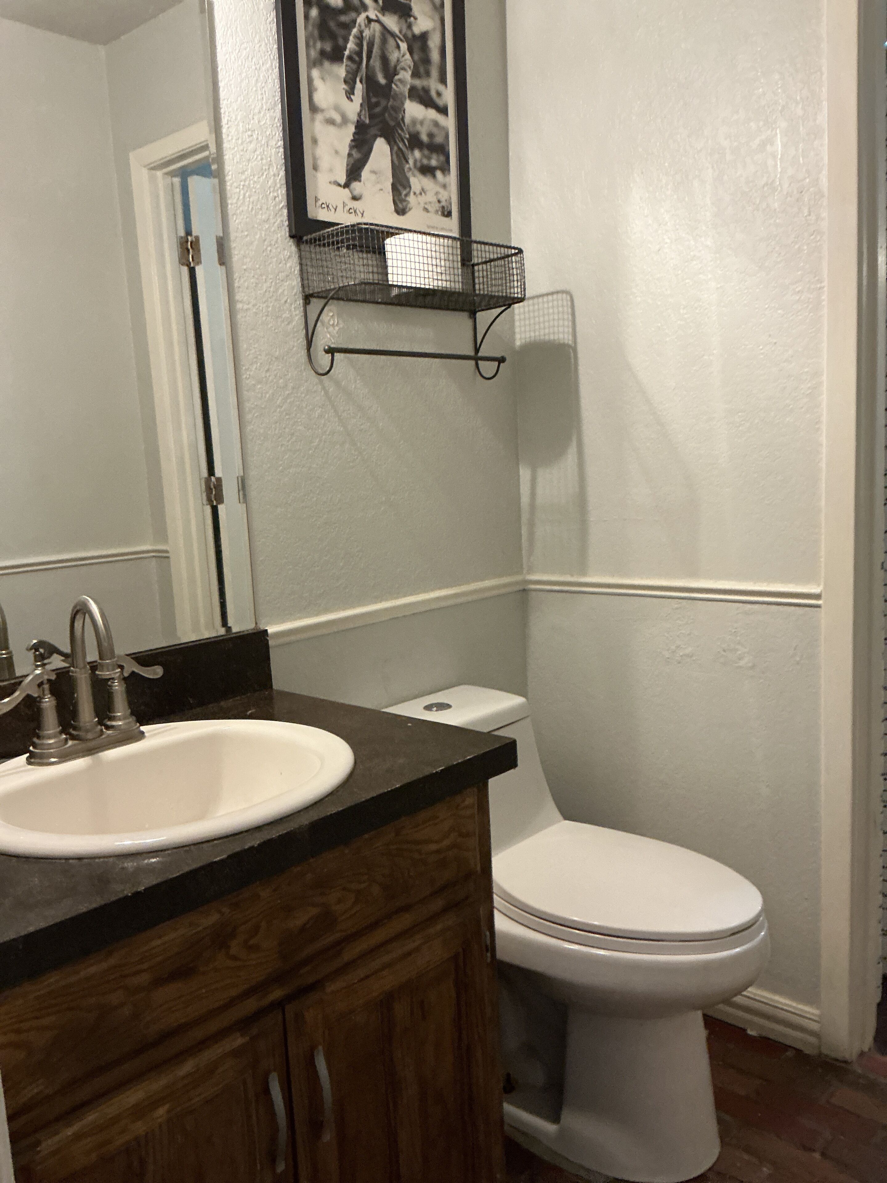 A bathroom with a white sink, wooden vanity, a toilet, and a framed picture on the wall.