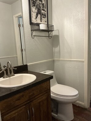 A bathroom with a white sink, wooden vanity, a toilet, and a framed picture on the wall. - Awesome 2-bedroom house with AC in charming KELLER ISD (Fort Worth)