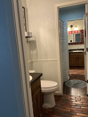 Un baño con un inodoro blanco, un tocador de madera, un perchero para toallas y una cortina de ducha.