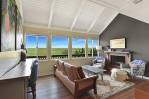 Ein geräumiges Wohnzimmer mit großem Fenster und Blick auf eine grüne Landschaft, einem Kamin und einer gemütlichen Sitzecke.