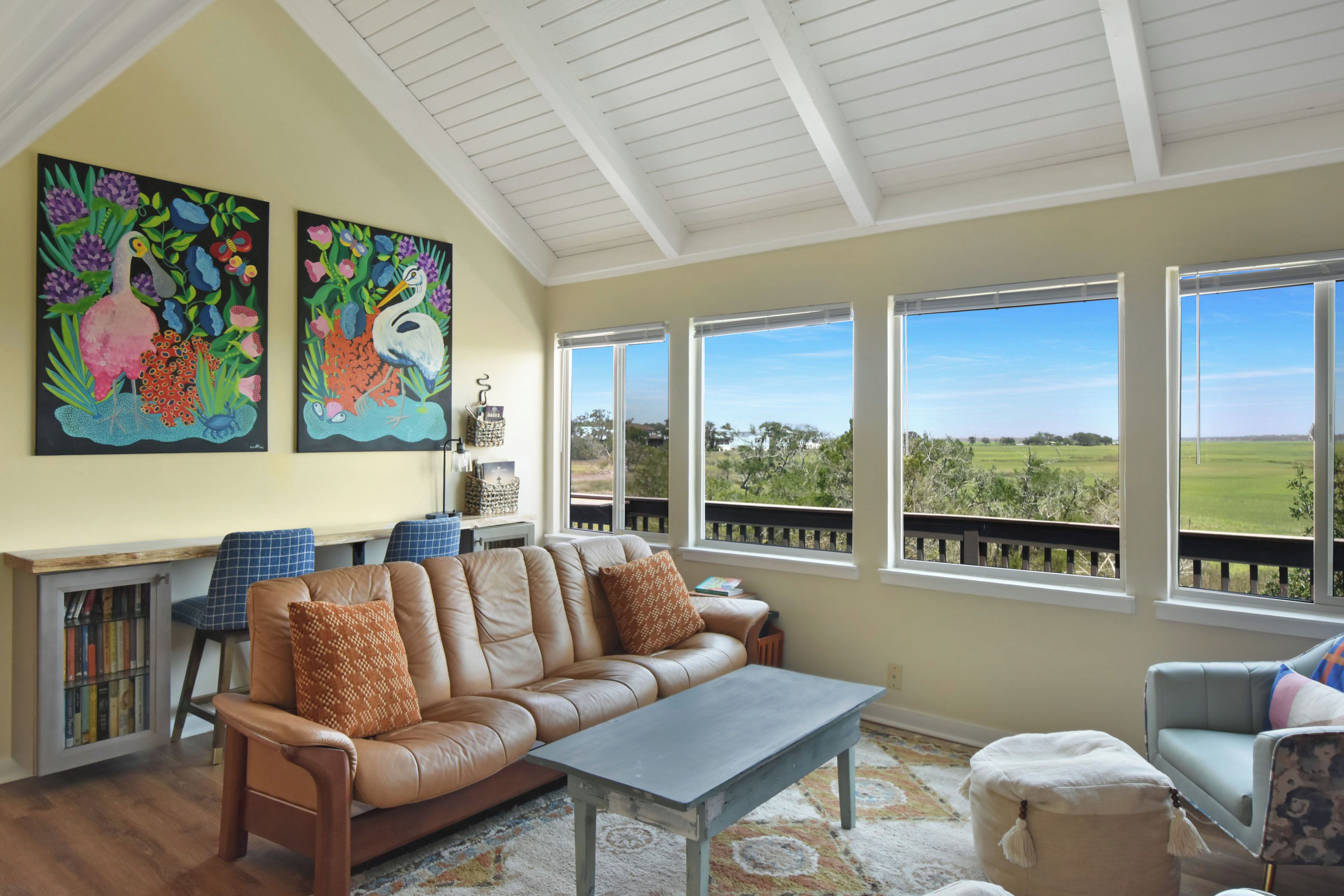 A spacious living room with a leather sofa, a coffee table, and a view of a green landscape through large windows.