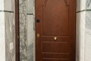 Una porta in legno con maniglia in ottone e una serratura, incastonata tra pareti in marmo.