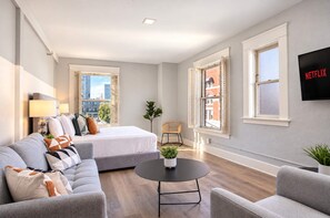A modern living room with a sofa, a bed, a round coffee table, and a TV mounted on the wall. - The Penn Hotel - Walk to Attractions & Sleeps 5!! (San Diego)