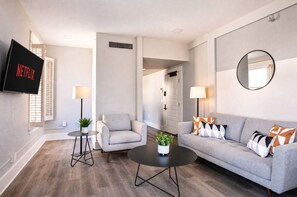 A modern living room with a grey sofa, two armchairs, a coffee table, and a TV mounted on the wall. - The Penn Hotel - Walk to Attractions & Sleeps 5!! (San Diego)