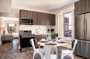 A modern kitchen with stainless steel appliances, a dining area with white chairs, and a view of the city through a window. - The Penn Hotel - Walk to Attractions & Sleeps 5!! (San Diego)