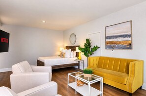 A modern hotel room with a bed, a sofa, a coffee table, and a TV screen displaying the Netflix logo. - The Penn Hotel - King & Queen Bed | Gaslamp Life (San Diego)