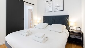 A hotel room with a bed, two bedside tables, a wall-mounted lamp, and two framed inspirational quotes. - Bonne Nouvelle Home - Appt 2 chambres proche gare (Paris)