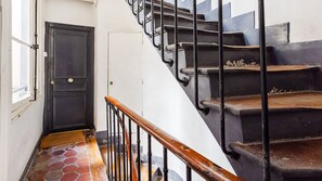 Eine Treppe mit Holzgeländer und schwarzen Metallspindeln, die zu einer dunklen Holztür mit runder Klinke führt.