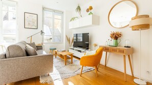 A modern living room with a sofa, coffee table, and a TV on a white cabinet. - Bonne Nouvelle Home - Appt 2 chambres proche gare (Paris)