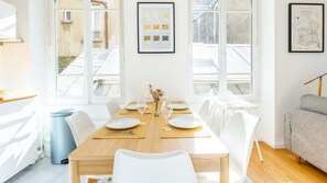 A dining area with a wooden table set for six, white chairs, and a vase with dried flowers. - Bonne Nouvelle Home - Appt 2 chambres proche gare (Paris)