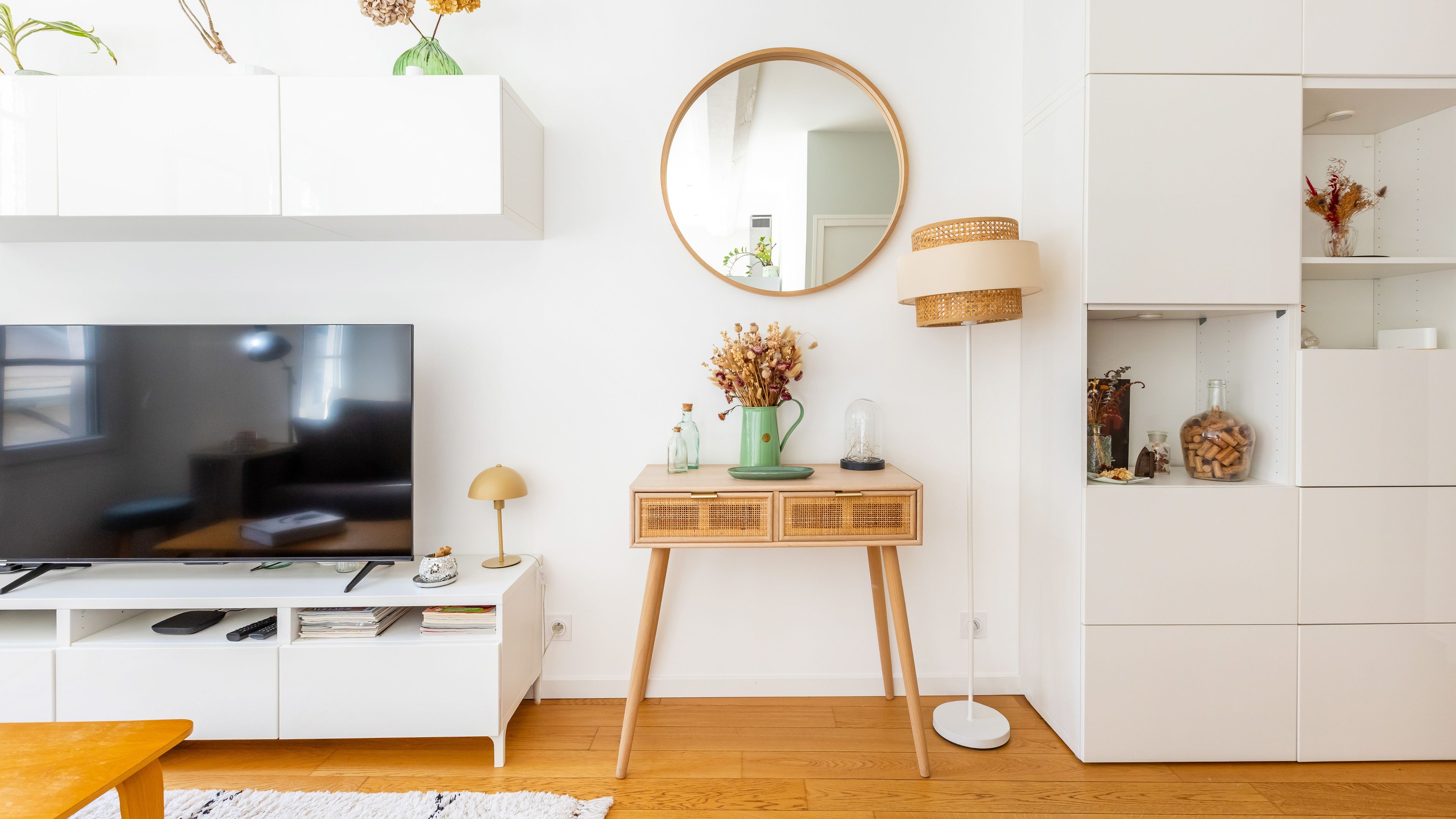 A modern living room with a flat-screen TV, a console table with decorative items, a floor lamp, and a white cabinet with shelves. - Bonne Nouvelle Home - Appt 2 chambres proche gare (Paris)