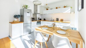 Una cocina moderna con armarios blancos, horno empotrado y un comedor con mesa de madera y sillas blancas.