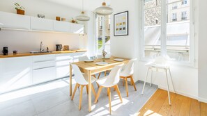 A modern kitchen with white cabinets, a wooden countertop, and a dining area with a table set for two. - Bonne Nouvelle Home - Appt 2 chambres proche gare (Paris)