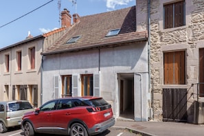 A red SUV parked in front of a stone building with a tiled roof and a small window. - Le 3 Saint-Blaise - Joli studio à Autun (Autun)